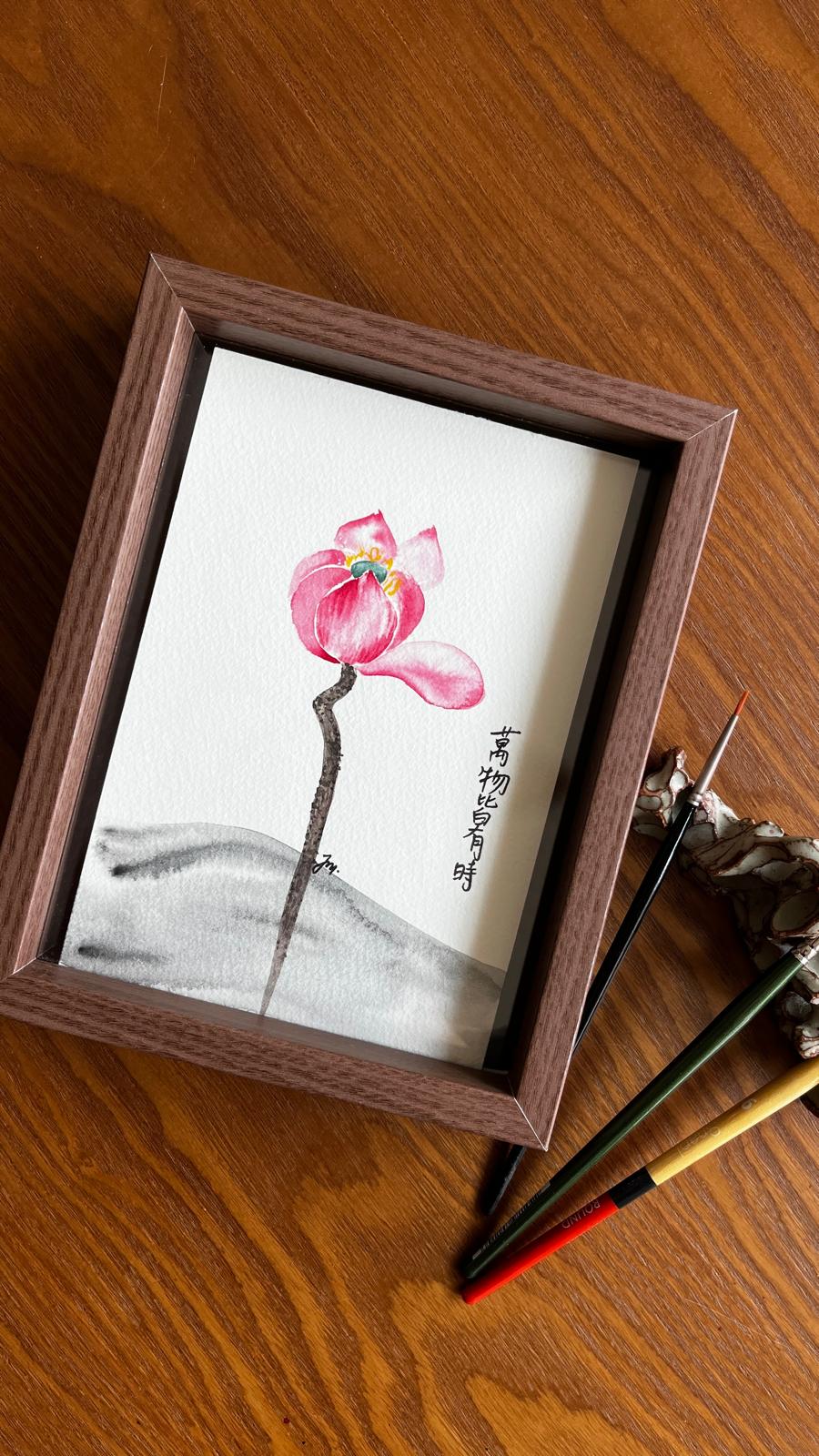 Framed watercolour painting of a pink Japanese Anemone with Chinese calligraphy, beside paintbrushes